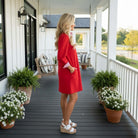 Model wearing the RED ALERT DRESS - Jodifl standing by a porch with flowers, showcasing its elegant design and confident style.