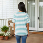Back view of a woman in the UNSTOPPABLE YOU TOP (aqua) with striped pattern, showcasing relaxed style on a porch.