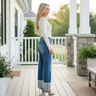 Model showcasing RISEN GIANNA JEANS with a high rise and wide cuff, styled in a relaxed fit on a porch.