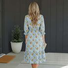 Woman showcasing the LIMITLESS LIVING MIDI DRESS with floral print and elastic waist, standing in a modern entryway.