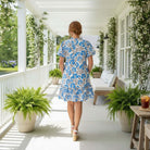 Cheerful Outlook Dress - Gigio in vibrant blue floral print, showcased outdoors on a sunny porch with ferns.