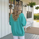 Model wearing LULU MAC Aqua with Coral Puff Logo Crew sweatshirt outdoors, showcasing a stylish back view.