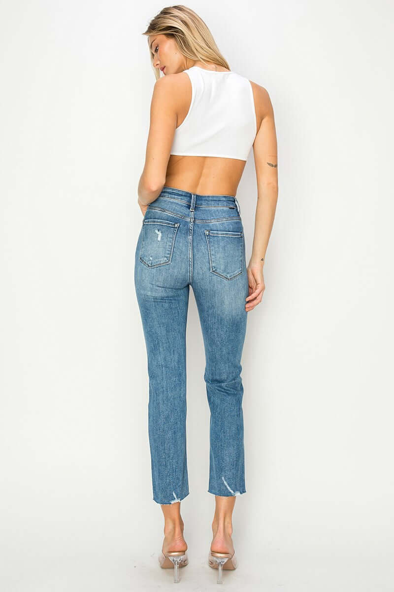 Back view of a woman wearing Risen Celeste high-rise distressed slim straight jeans with a cropped top.
