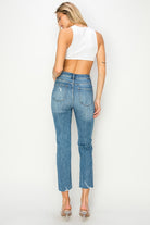 Back view of a woman wearing Risen Celeste high-rise distressed slim straight jeans with a cropped white top.