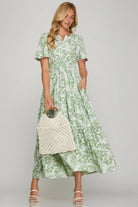 Woman in sage floral maxi dress with flutter sleeves and side pockets, holding a woven bag.