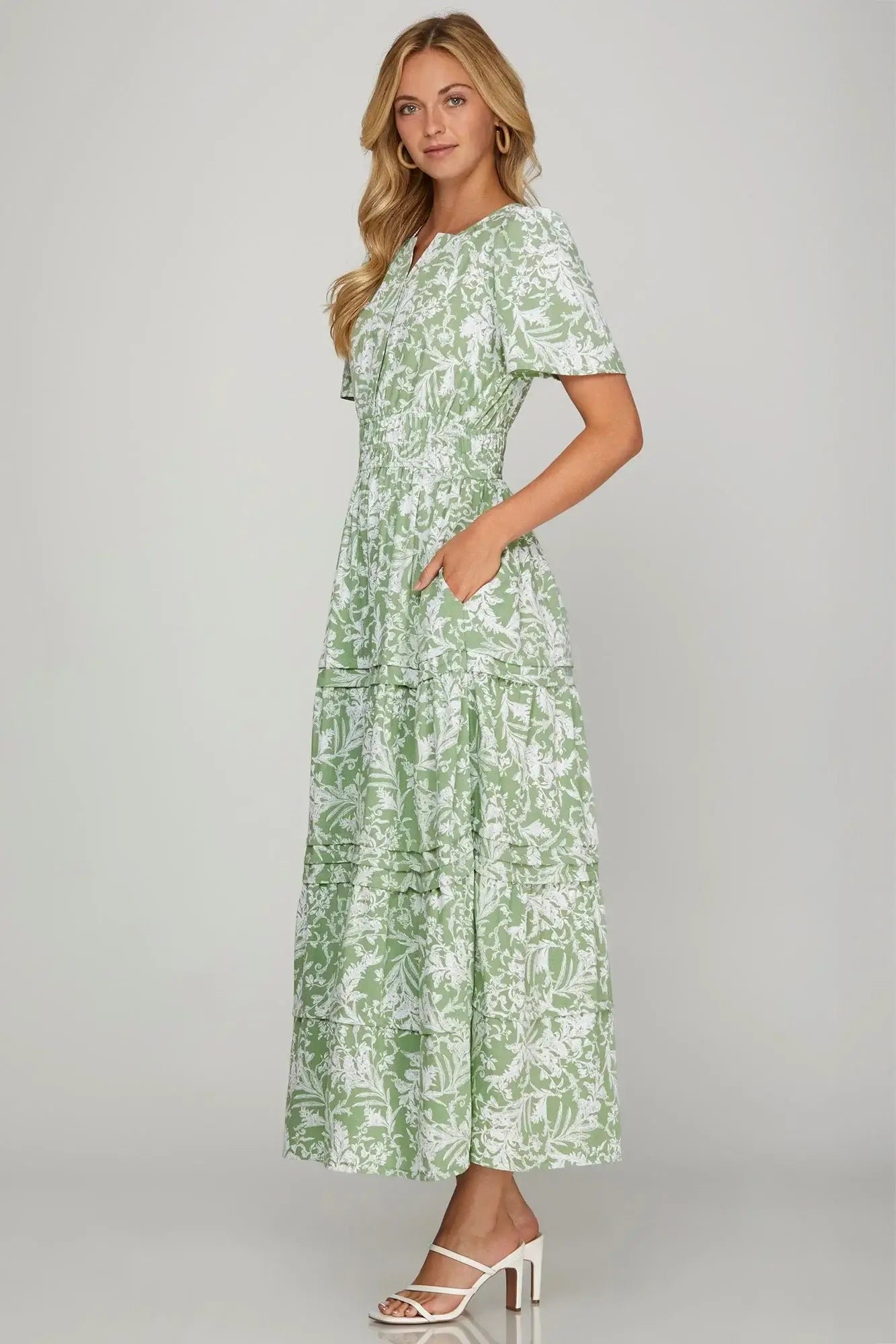 Model wearing the Meadow Moments Dress by She + Sky, showcasing a floral pattern in sage with flutter sleeves and pockets.