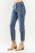 Judy Blue Janie Plus Size Joggers in medium wash with cuffed hems and elastic drawstring waist, paired with ankle boots.
