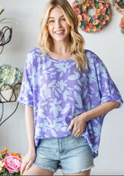 Model wearing the Violet Vacations top by Hopely, featuring a floral print and oversized fit, styled with denim shorts.