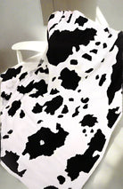 Black and white cow-patterned Cozy Cow Blanket by Howdy Honey draped over a chair, ultra-soft and perfect for adding charm and warmth.