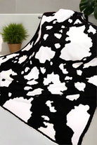 Black and white cow-patterned cozy blanket draped over a sofa, enhancing room decor with warmth by Howdy Honey.