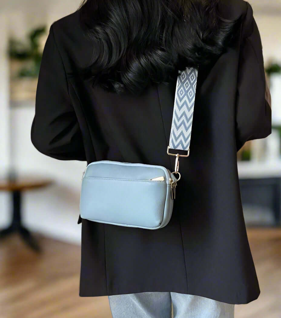 SKYE Crossbody Bag in light blue with patterned strap, worn casually with a black jacket, showcasing stylish functionality.