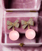 Laced Atmosphere Earrings featuring rhinestone bows and cool pink dangling spheres in a luxurious jewelry box.