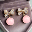 Laced Atmo-Sphere earrings with rhinestone bows and pink dangling spheres, showcasing glamorous jewelry design.