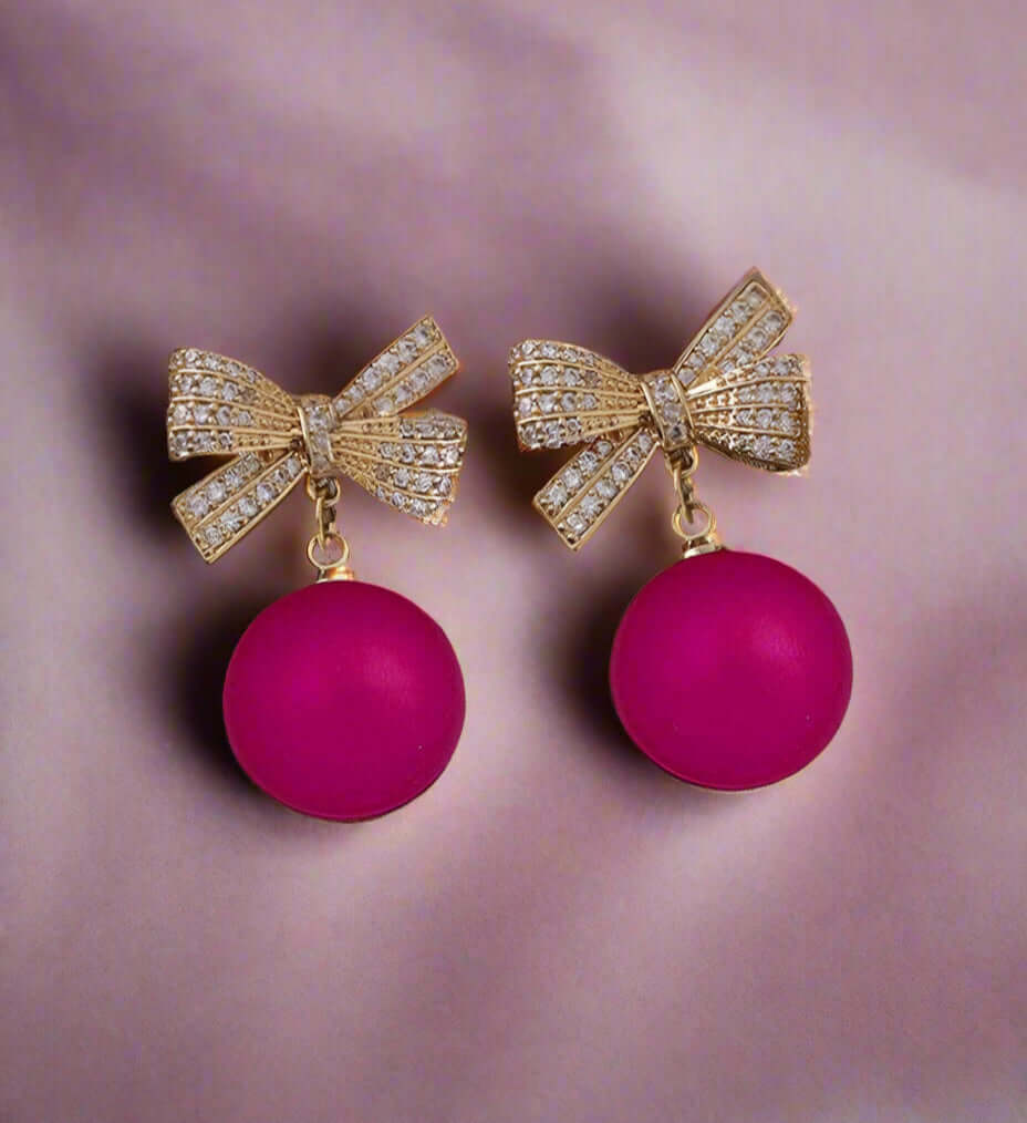 LACED ATMO-SPHERE EARRINGS in hot pink featuring rhinestone bows and dangling spheres, perfect for a glamorous look.