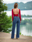 Fashion model wearing JUDY BLUE Mia dark wash wide leg jeans with a backless red top, showcasing a scenic lake backdrop.