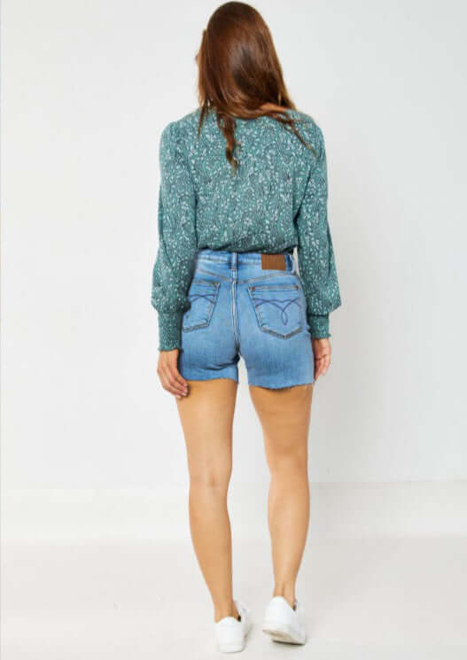 Back view of a woman wearing JUDY BLUE Cassidy Shorts paired with a floral green shirt and white sneakers.