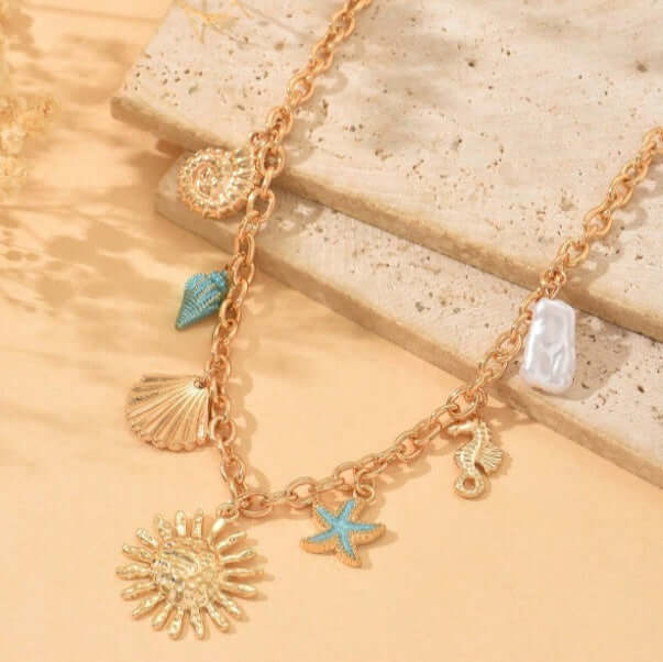 Golden Sunseeker Charm Necklace with seashells, seahorse, starfish, and pearl accents on sandy background.