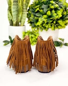 Copper brown Rodeo Girl boots with fringe by Very G, showcasing faux suede texture and back view, surrounded by green plants.