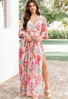 Elegant woman in Tropical Sensation Dress with high slit and floral design, perfect for summer occasions.