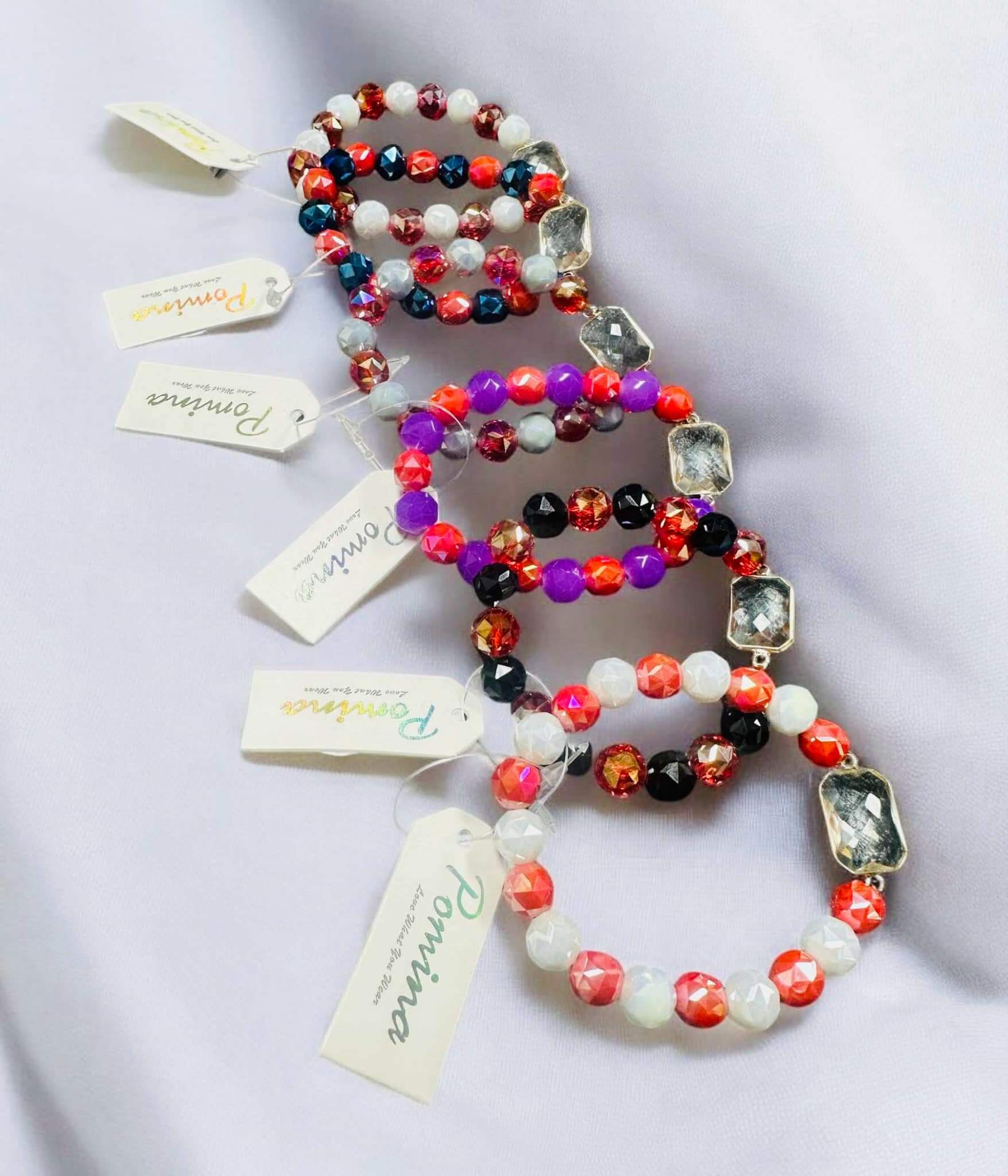 Colorful stackable Pomina bracelets featuring glass gemstones in vibrant hues and gold-tone accents.