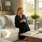 Model wearing GRACEFUL INSTINCTS MAXI DRESS, sitting on a couch with a coffee mug in a cozy living room setting.