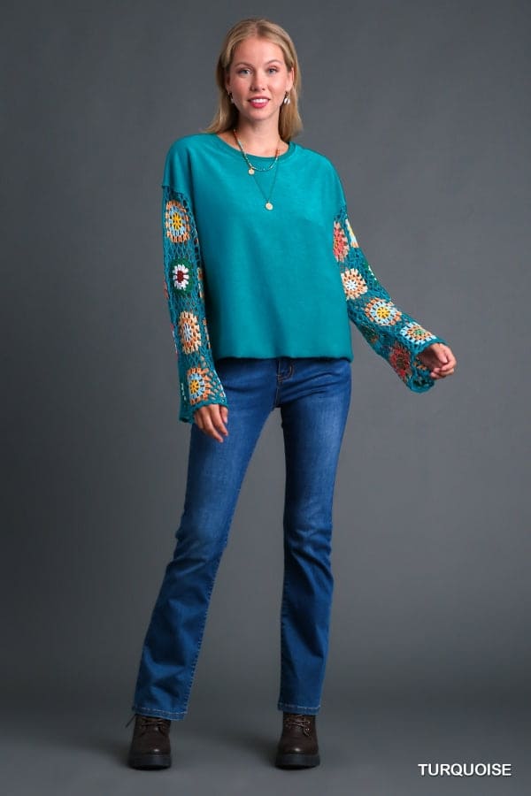 Woman wearing Flower Child Crochet Sleeve Top with colorful hand-knit details and turquoise fabric, paired with blue jeans.