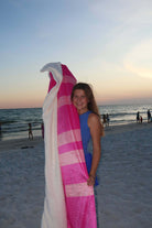 Girl holding LM-BK LULU MAC BLANKET PINK at the beach, enjoying sunset and warmth.
