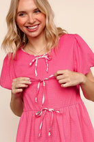 Smiling woman in a pink RibbonS & Beaus Top with ribbon details and flutter sleeves.