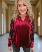 Woman wearing Umgee burgundy velvet top with black lace sleeves, V-neck, and ruffled collar in elegant setting.