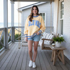Model wearing LULU MAC SOCIAL SOCIETY CREW (Butter/Cornflower) sweatshirt on a porch with ocean view.