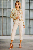 Woman wearing WARM EMBRACE Jacket by Umgee in pistachio and tan plaid, styled with neutral pants and heels in an urban setting.