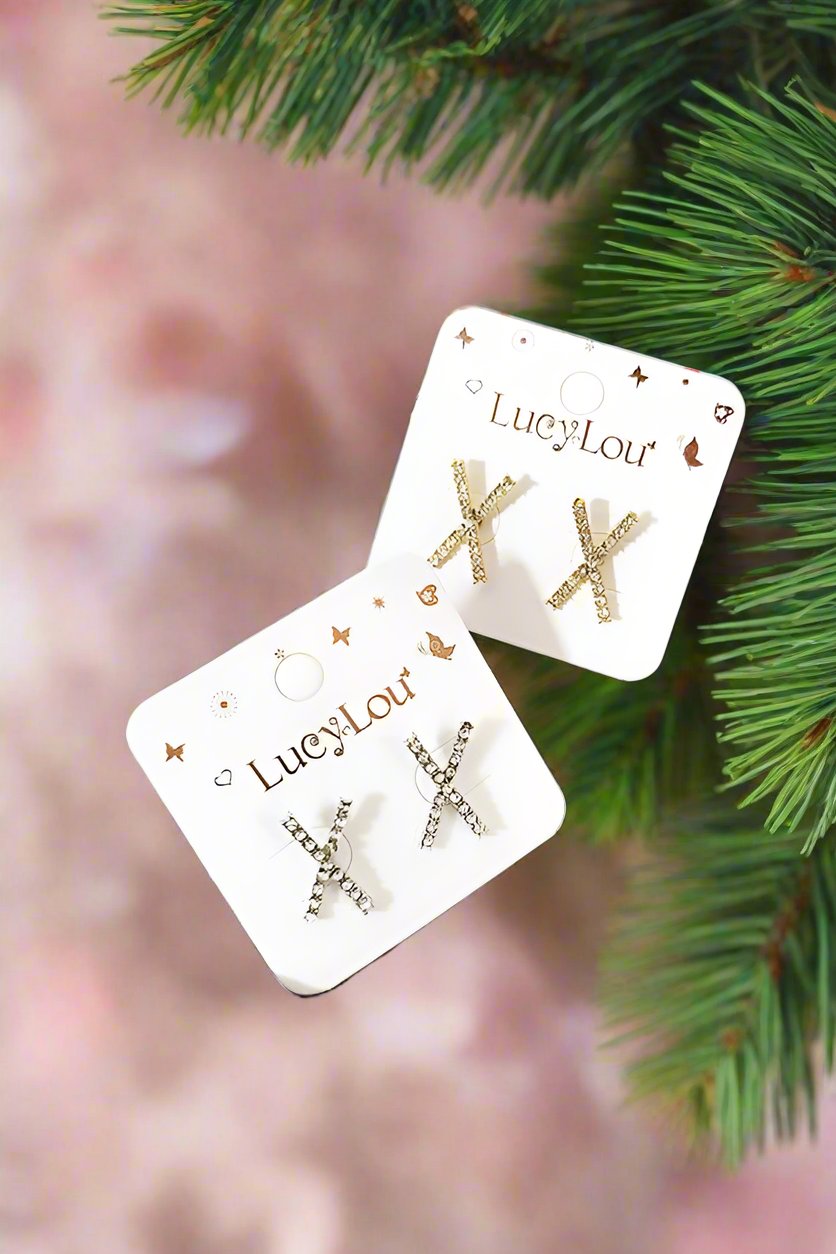 X Stud Earrings on display, featuring assorted designs in a stylish setting with a wooden tray and decor.