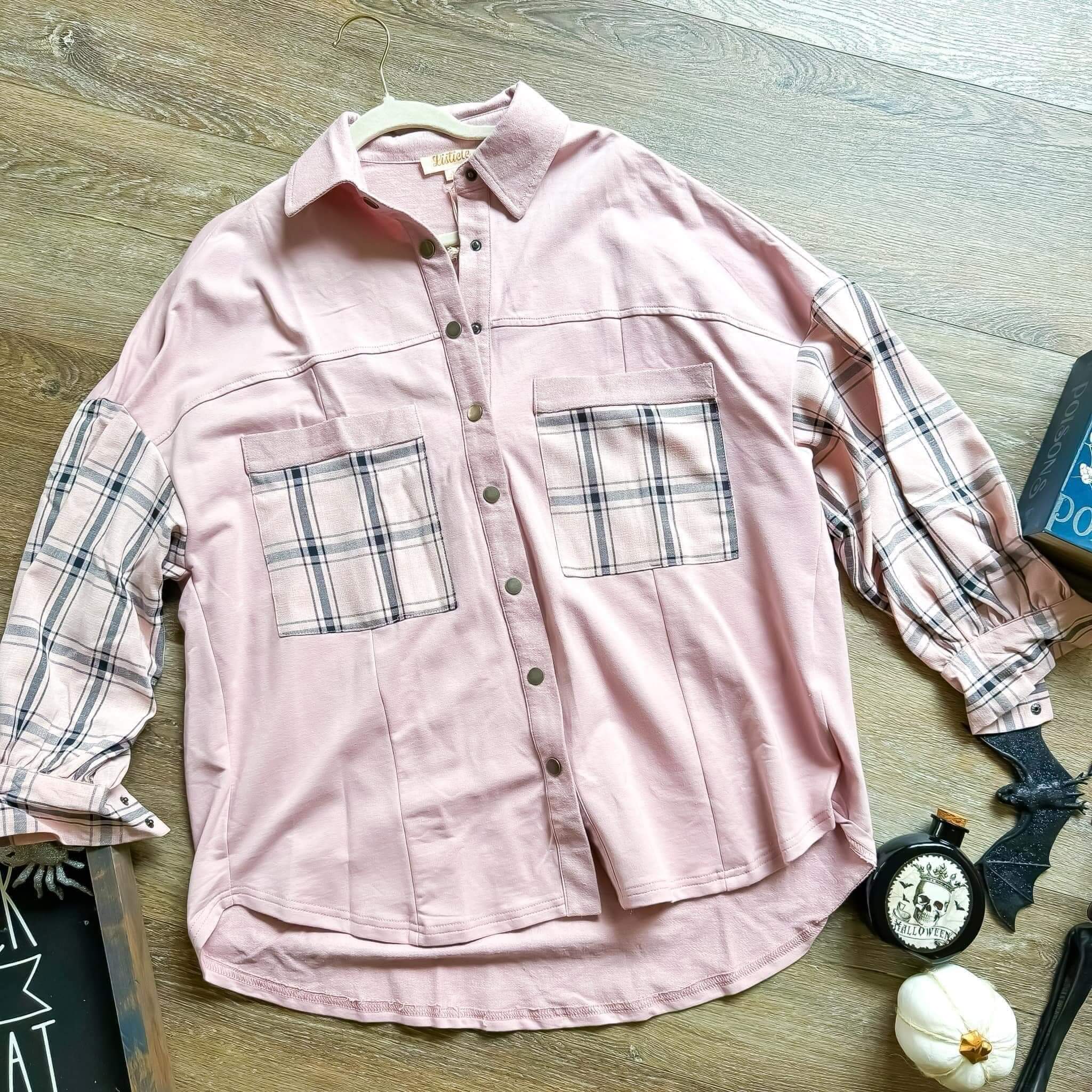 Light pink Listicle top with plaid sleeves and pockets, featuring a snap-up front, displayed on a wooden surface.