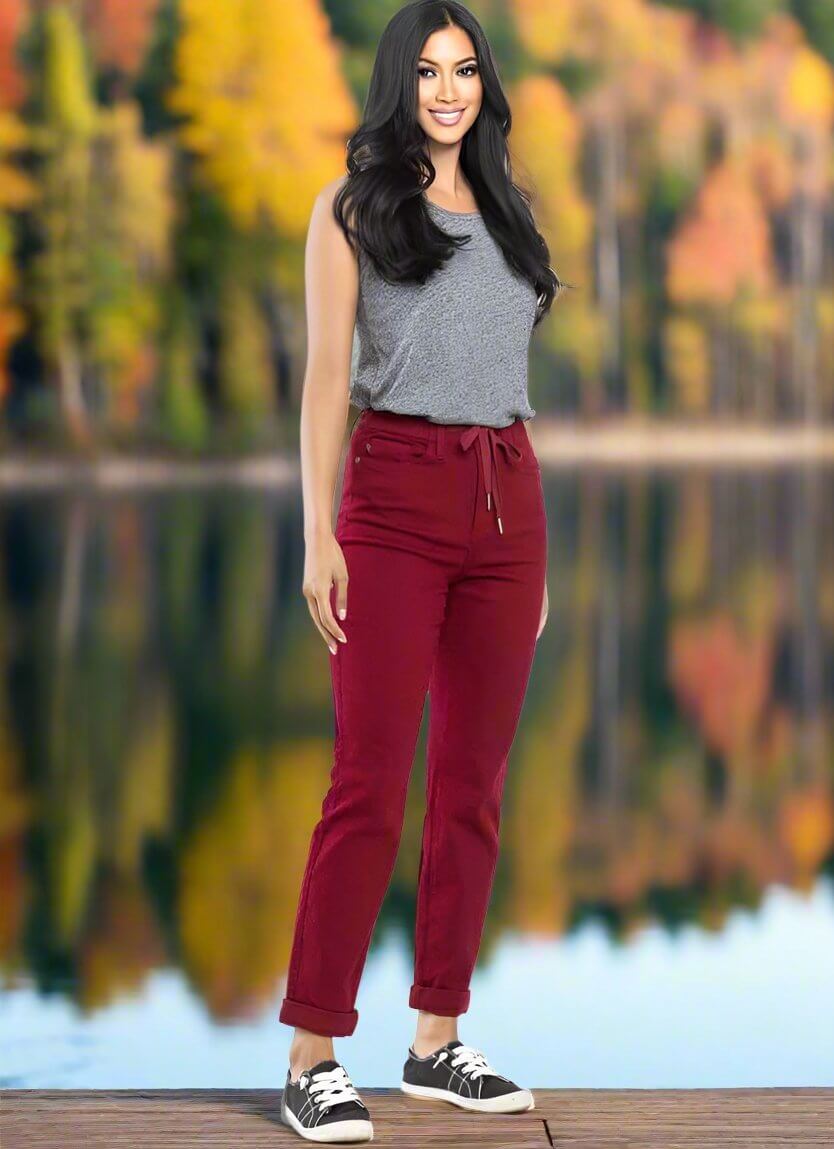 Woman wearing Judy Blue Bridget Joggers in crimson with drawstring waist, standing by a lake in autumn.