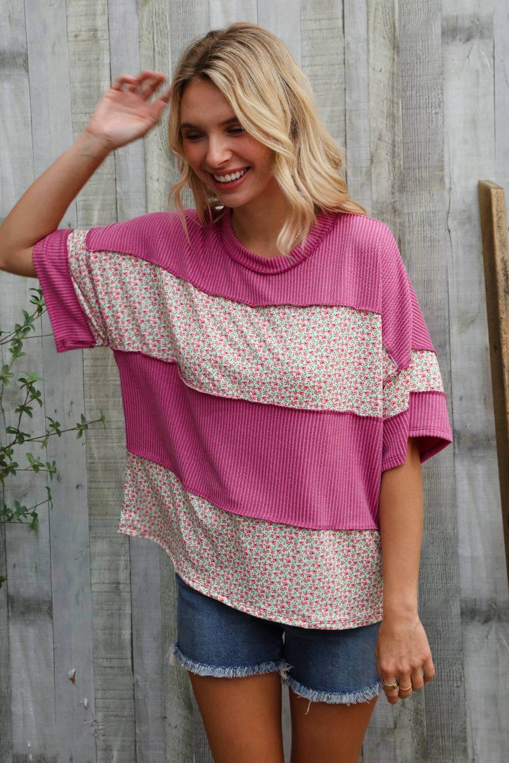 Woman wearing a fuchsia floral color block wavy rib pullover with shorts in a relaxed outdoor setting.
