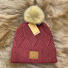 Burgundy pom pom beanie with faux fur detail and diagonal pattern by C.C. on a plush fur background.