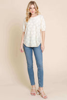 Model wearing the Field of Daisies Top in cream, featuring puff sleeves and textured daisy embroidery, styled with jeans.