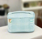 Light blue textured cosmetic bag with a gold zipper and side pocket, perfect for organizing personal items.