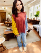 Woman wearing TRAVELING LIGHT top by BiBi in burgundy, gold, and blue color block with long sleeves and crew neck in cozy living room.