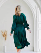 Elegant woman wearing dark green midi dress with smocked sleeves and waist, showcasing timeless style and comfort in a stylish setting.