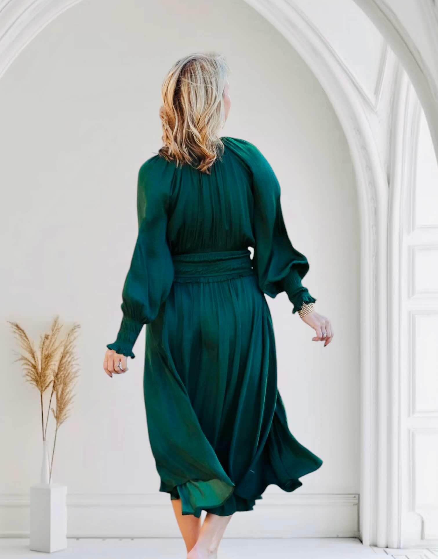 Elegant woman wearing dark green midi dress with smocked sleeves and waist, showcasing timeless style and comfort in a stylish setting.