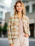 Woman wearing WARM EMBRACE Jacket by Umgee in pistachio plaid, featuring tortoise shell buttons, paired with a neutral top and beige pants.