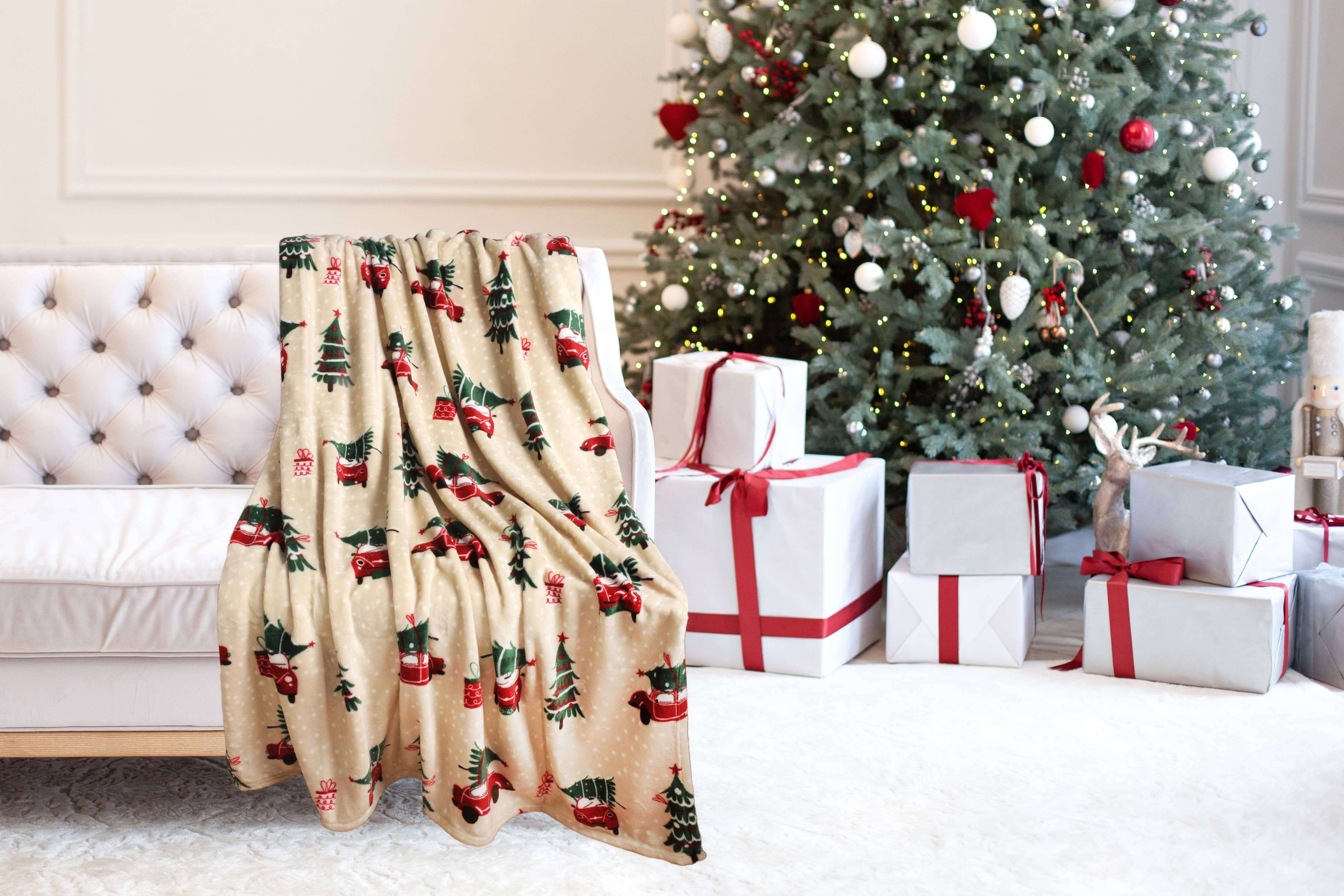 Christmas Cheer Plush Throw Blanket by Kathy Ireland on sofa, festive holiday design with Christmas tree and gifts in living room.