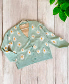 Teal Daisy Dreamer Cardigan with white daisies and button front on wooden background, made of 60% cotton and 40% acrylic.