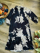 Black and white floral midi dress by Umgee with long sleeves, hi/low hem, and tiered ruffle, displayed on wooden floor.