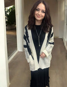 Woman wearing an ivory and black Ultra Soft Cardigan with fuzzy texture and pockets over a black dress, smiling indoors.