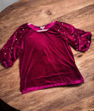 Scarlet velvet top with pearl-accented sleeves by Umgee, displayed on a wooden surface. Luxurious texture, deep magenta hue.