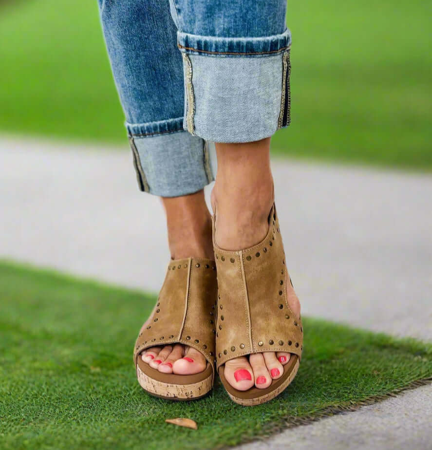 Tan Corkys Carley studded wedges on feet, showcasing a comfortable slingback design and cork wedge heel.