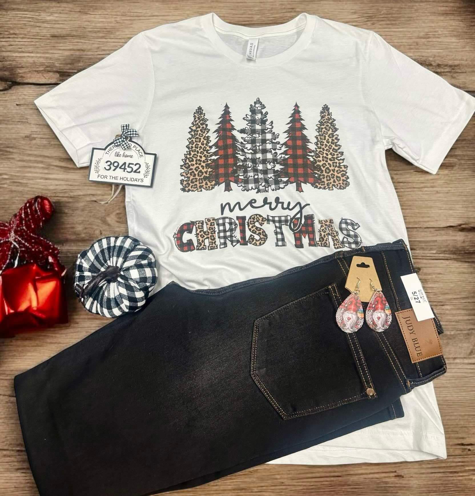 White Bella Canvas Wild Merry Christmas Tee with leopard and plaid trees, paired with black jeans and festive red ornaments.