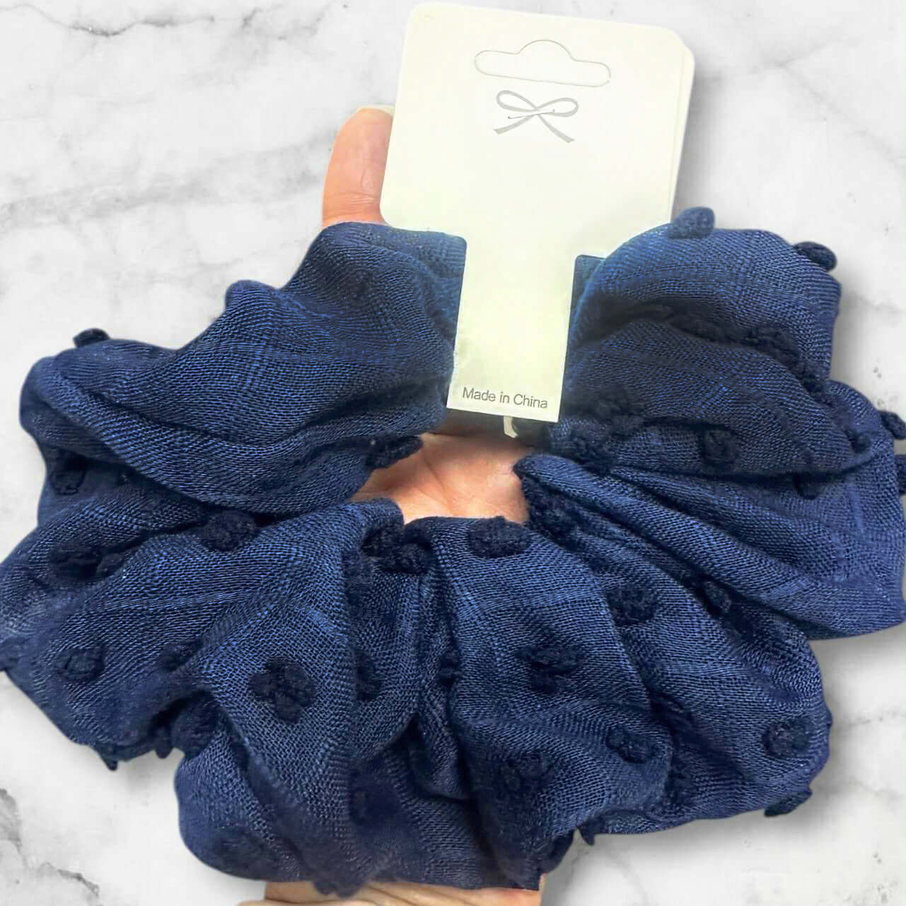 Navy blue pompom textured scrunchie held in hand, perfect for stylish hair accessories or wrist wear.